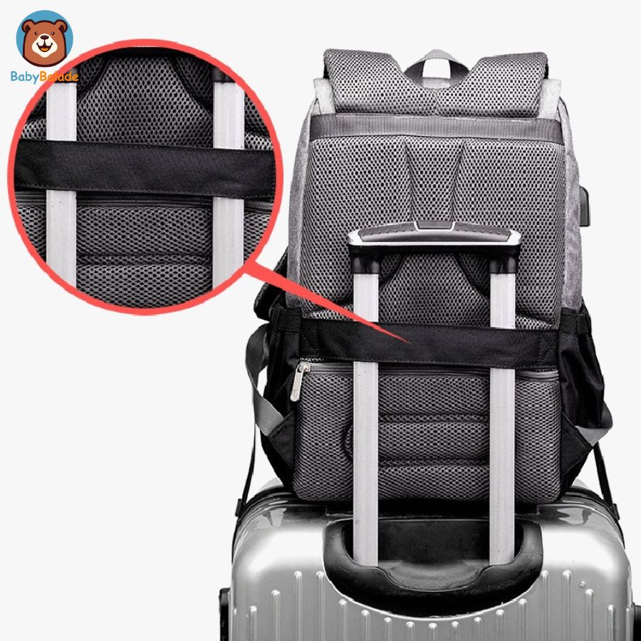 sac à dos à langer de couleur gris accroché sur une valise